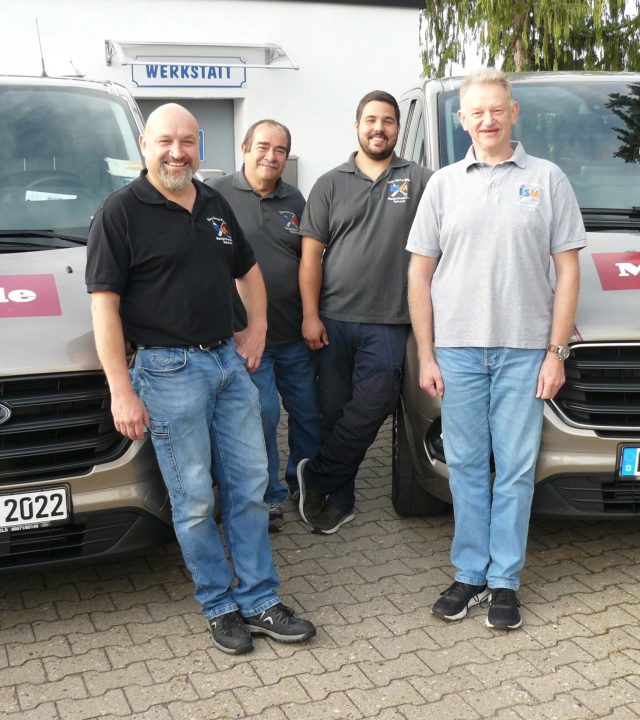 Das Team von Elektroservice Müller. 4 Personen stehen vor den 2 Firmenfahrzeugen.